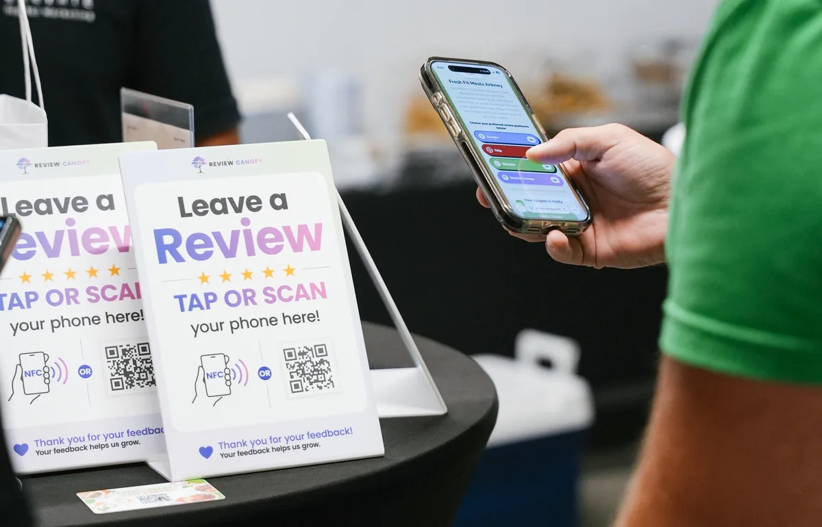 A phone displaying a customized review page beside Review Canopy tap-or-scan stands